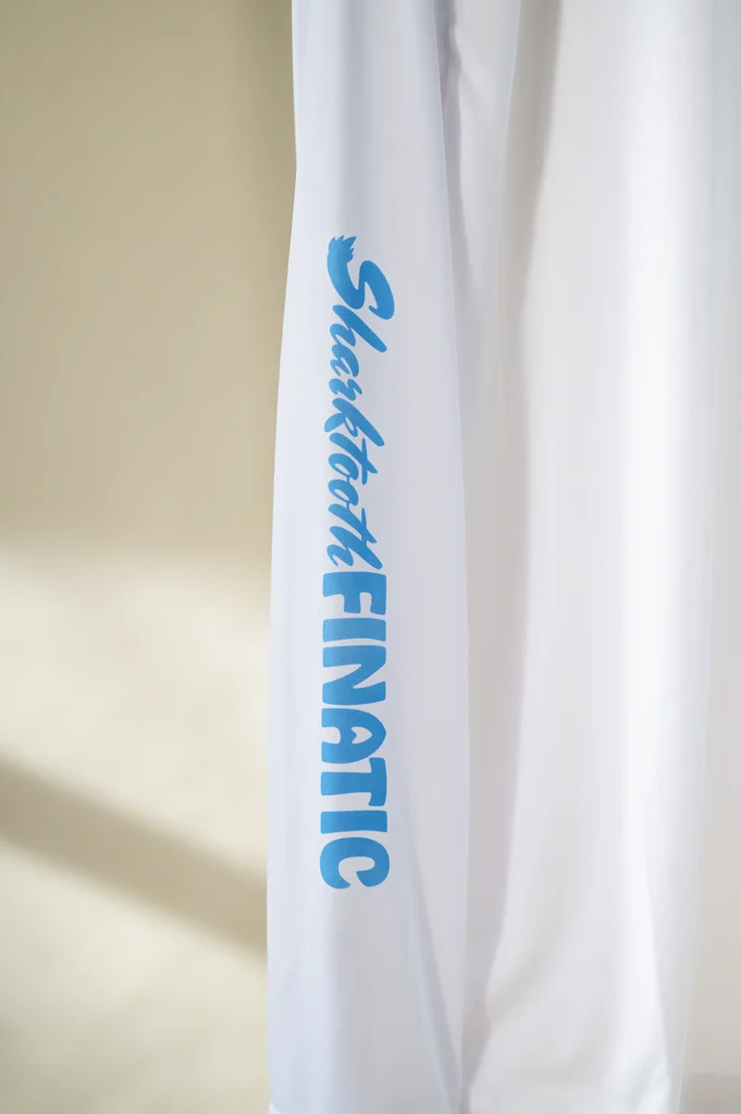 white performance long-sleeve shirt with blue logo and koi pond great white shark tooth design on the sleeve