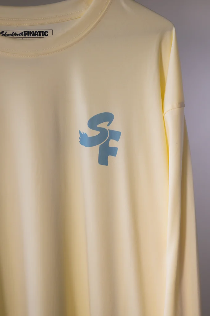 butter yellow performance long-sleeve shirt with blue logo and koi pond great white shark tooth design on the sleeve
